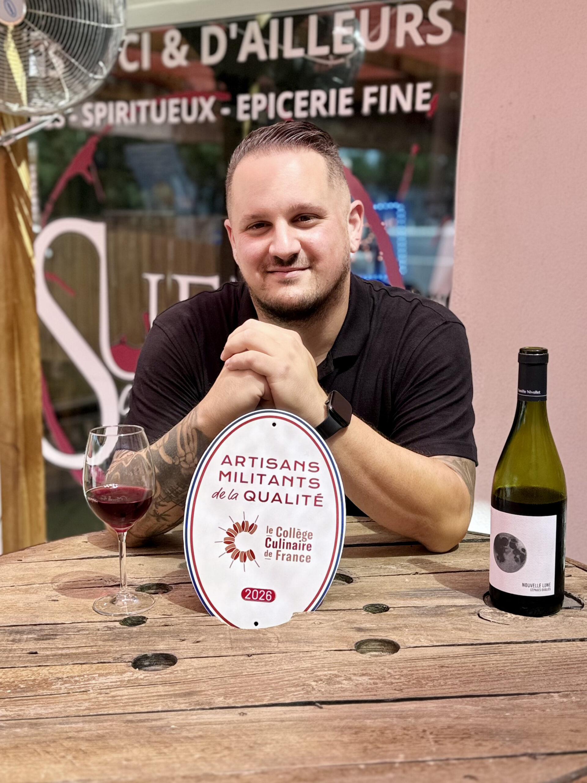 Florian, gérant et caviste de Sueño à Quissac, avec la plaque Artisan Militant de la Qualité
